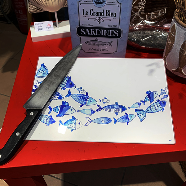 Planche à découper blanche avec un banc de poissons bleu et avec 1 couteau posé dessus